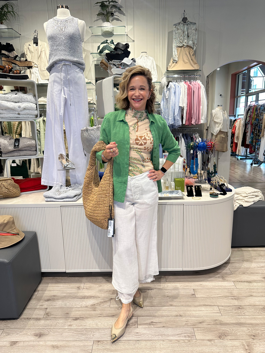 Capsule 4 Store owner in a green shirt and white pants stands by a rack of luxury clothing at Fringe & Form boutique.