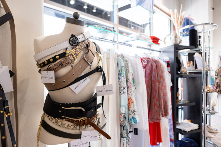 Display of stylish belts inside Fringe & Form with metallic buckles drape a mannequin figure.