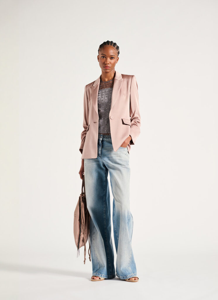 Louisa Cerano Jeans and Jacket A model in Luisa Cerano brand clothing a light pink blazer with casual jeans stands against a white wall.