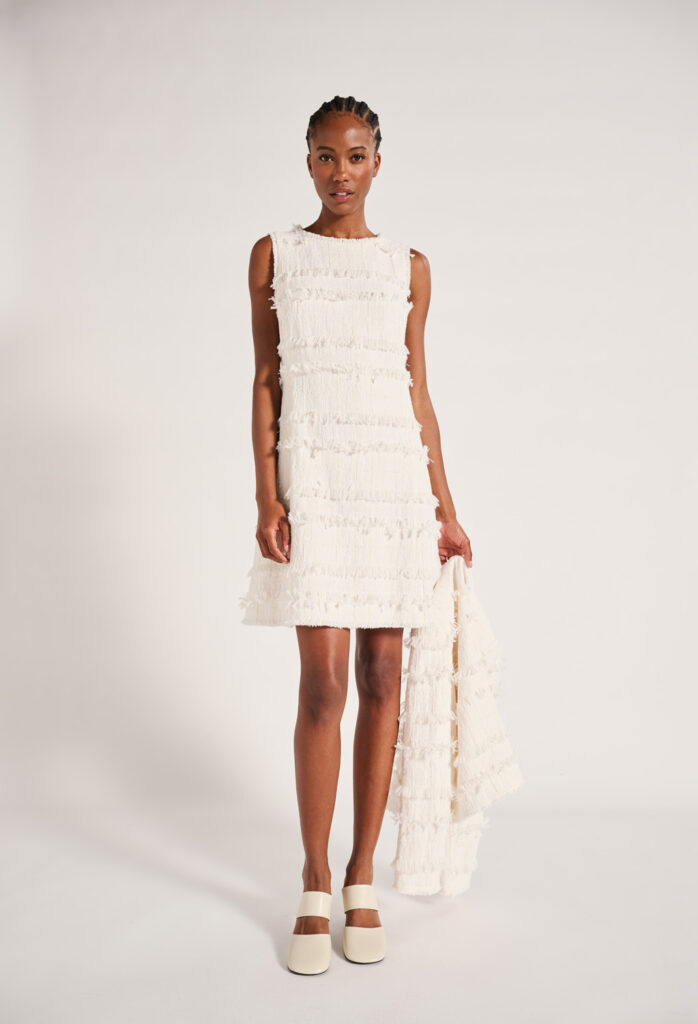 Luisa Cerano Dress and Jacket A woman stands wearing a white dress with fringe and holds a matching jacket.