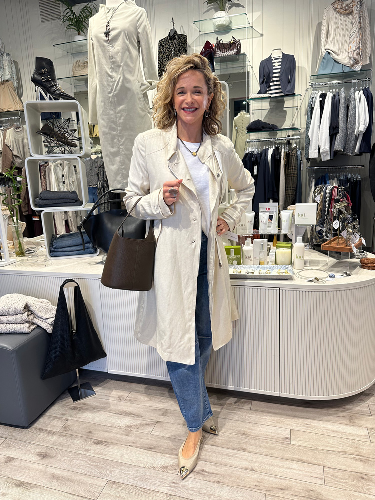 Fringe & Form store owner Michelle poses in a white jacket and jeans with a black bag.
